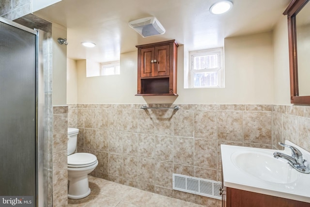 bathroom with toilet, tile patterned floors, vanity, tile walls, and a shower with shower door