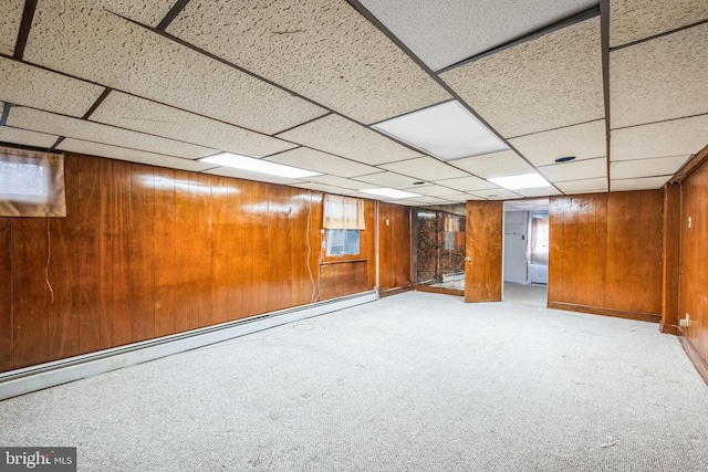 basement featuring wooden walls, a baseboard radiator, a paneled ceiling, and light carpet