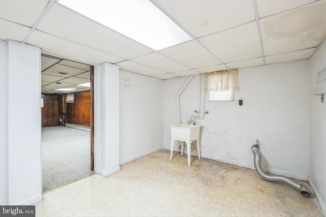 basement with baseboard heating, light colored carpet, a drop ceiling, and wooden walls