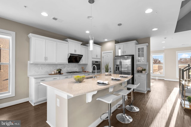 kitchen featuring decorative light fixtures, an island with sink, stainless steel appliances, decorative backsplash, and white cabinetry