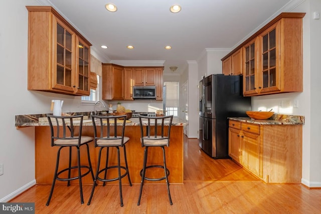 kitchen with kitchen peninsula, crown molding, a kitchen bar, appliances with stainless steel finishes, and light wood-type flooring