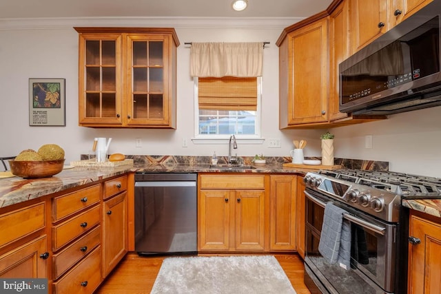 kitchen with stone counters, appliances with stainless steel finishes, crown molding, and sink