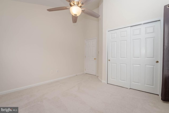 unfurnished bedroom with ceiling fan, light colored carpet, a high ceiling, and a closet