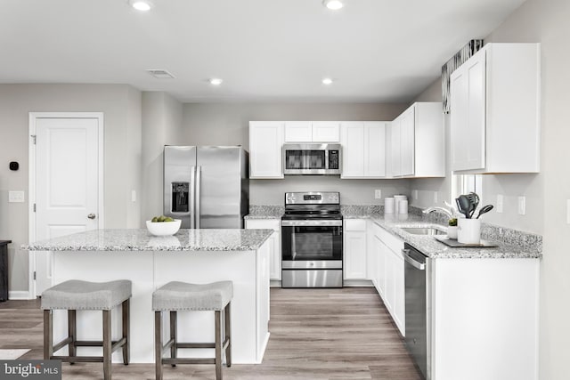 kitchen featuring white cabinets, a kitchen island, appliances with stainless steel finishes, and light hardwood / wood-style flooring