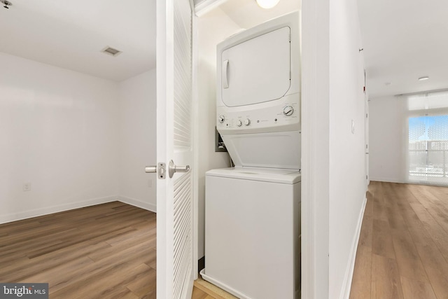 laundry room featuring hardwood / wood-style floors and stacked washing maching and dryer