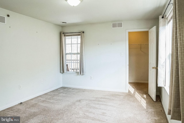 unfurnished bedroom featuring a spacious closet, light carpet, and a closet