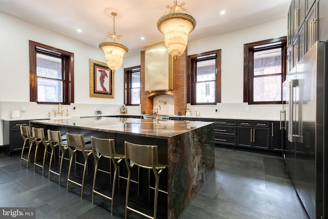 kitchen featuring stone countertops, high quality fridge, decorative light fixtures, a kitchen bar, and a center island