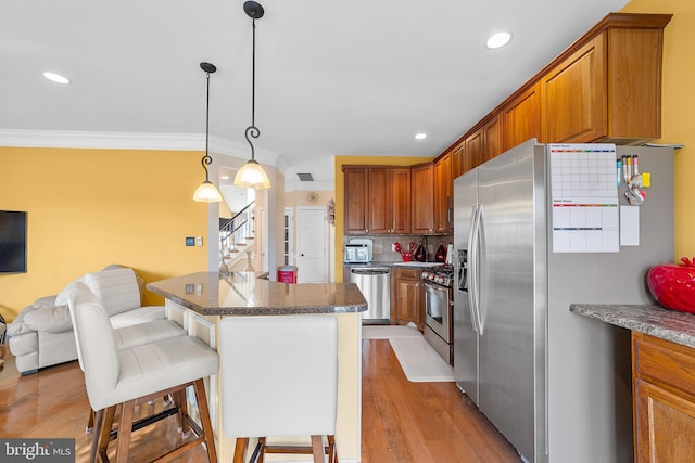 kitchen with hanging light fixtures, light wood-type flooring, ornamental molding, appliances with stainless steel finishes, and a kitchen bar