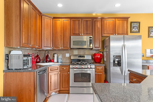 kitchen featuring decorative backsplash, stainless steel appliances, dark stone counters, and sink