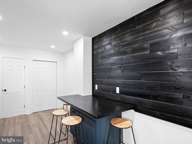 bar with hardwood / wood-style floors, wood walls, and blue cabinetry