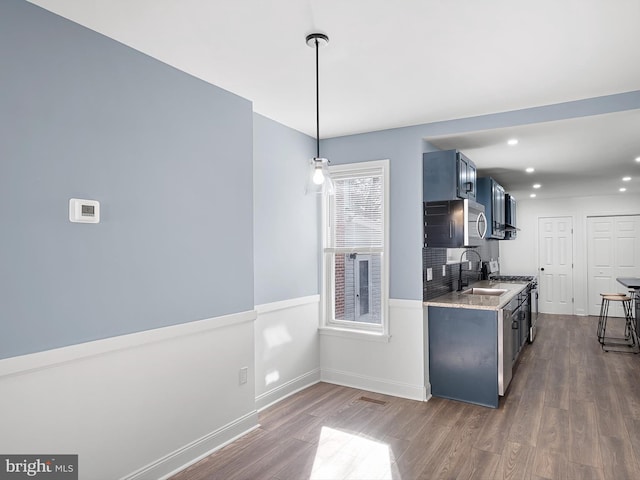 kitchen with light stone countertops, appliances with stainless steel finishes, dark wood-type flooring, sink, and decorative light fixtures