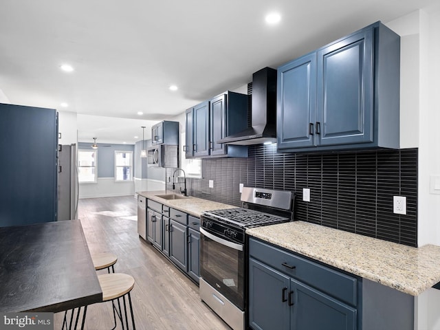 kitchen featuring sink, light hardwood / wood-style flooring, wall chimney exhaust hood, ceiling fan, and stainless steel appliances