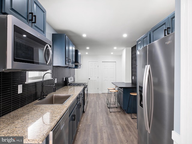 kitchen with decorative backsplash, appliances with stainless steel finishes, sink, blue cabinetry, and hardwood / wood-style floors