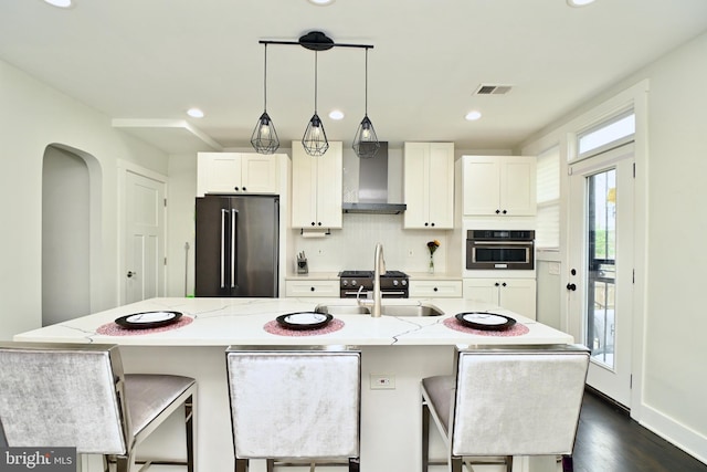 kitchen featuring wall chimney range hood, an island with sink, and appliances with stainless steel finishes