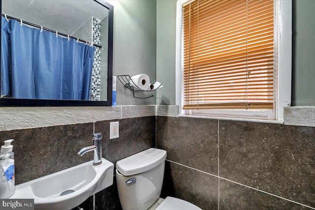 bathroom featuring toilet, tile walls, and sink