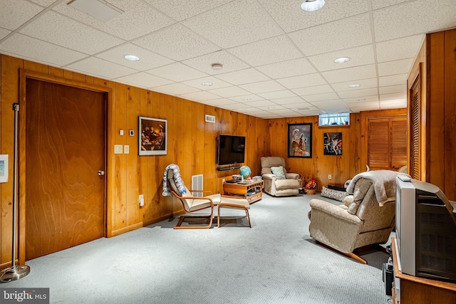 living room with carpet, a paneled ceiling, and wood walls