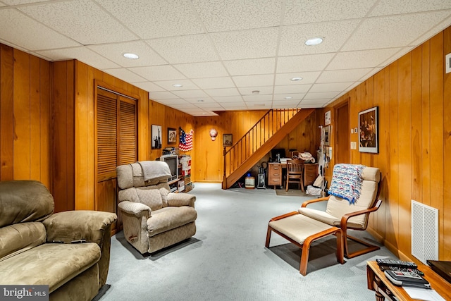 living room with wood walls, light carpet, and a drop ceiling