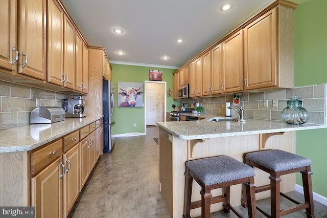 kitchen featuring a kitchen bar, kitchen peninsula, light stone countertops, stainless steel appliances, and sink