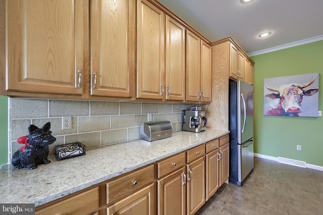 kitchen featuring crown molding, stainless steel fridge, light stone counters, and backsplash