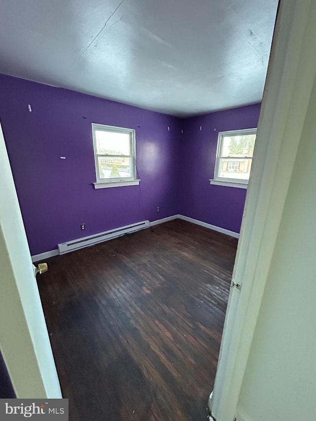 empty room featuring dark wood-type flooring, a wealth of natural light, and a baseboard heating unit