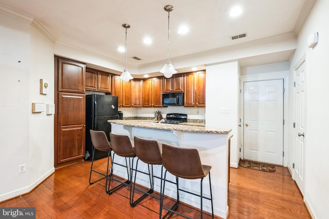 kitchen featuring pendant lighting, black appliances, light stone counters, a breakfast bar, and a center island with sink