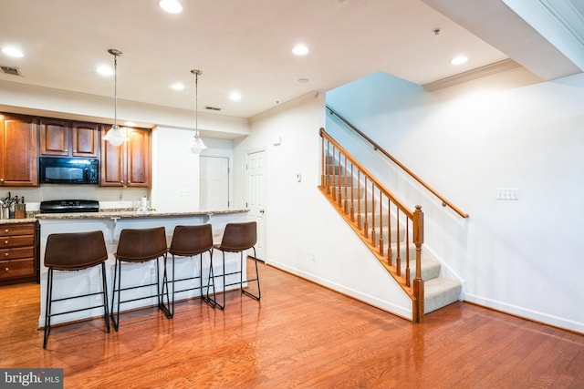 kitchen featuring a breakfast bar area, decorative light fixtures, ornamental molding, and light stone countertops