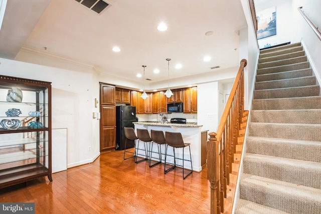 kitchen featuring light stone countertops, black appliances, decorative light fixtures, hardwood / wood-style flooring, and a breakfast bar area