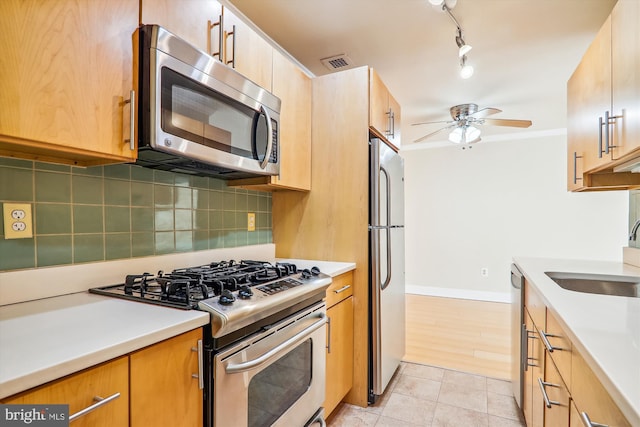 kitchen with appliances with stainless steel finishes, light tile patterned floors, ceiling fan, sink, and backsplash