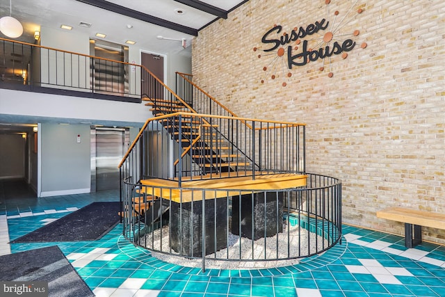 stairway featuring a high ceiling, elevator, tile patterned floors, and brick wall