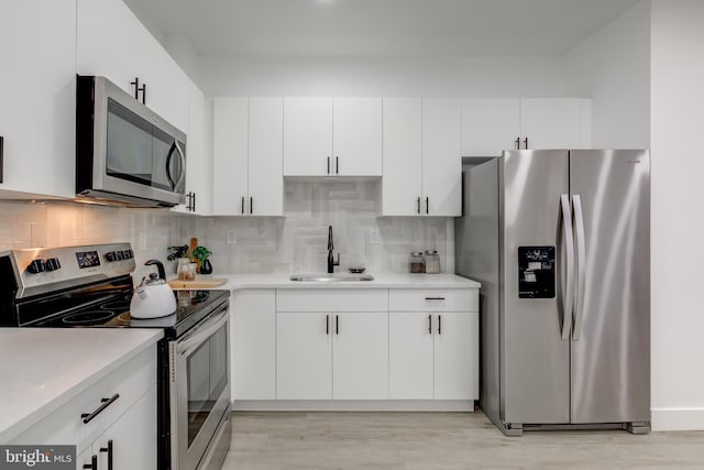 kitchen with sink, white cabinets, light wood-type flooring, backsplash, and appliances with stainless steel finishes