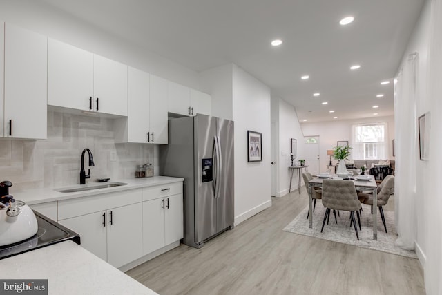 kitchen with sink, white cabinetry, light wood-type flooring, and stainless steel refrigerator with ice dispenser