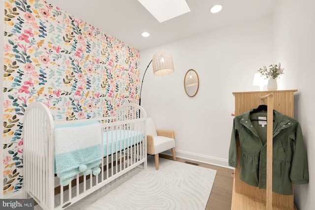 bedroom with a nursery area, wood-type flooring, and a skylight