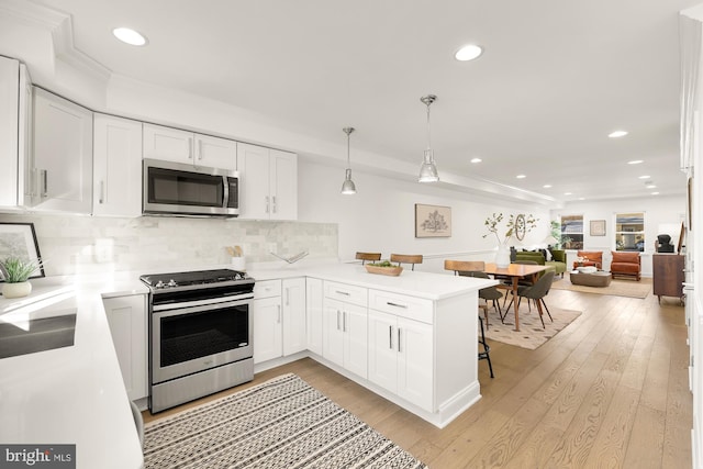 kitchen featuring hanging light fixtures, tasteful backsplash, kitchen peninsula, white cabinets, and appliances with stainless steel finishes