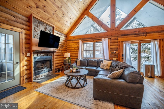 living room featuring a healthy amount of sunlight, high vaulted ceiling, rustic walls, and a stone fireplace