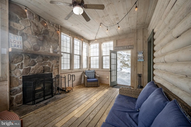 interior space featuring a stone fireplace, wooden ceiling, wood-type flooring, wooden walls, and ceiling fan