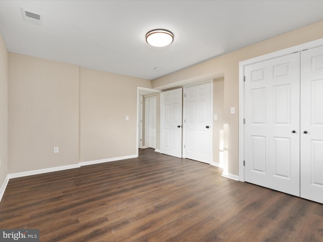 unfurnished bedroom with dark wood-type flooring and multiple closets