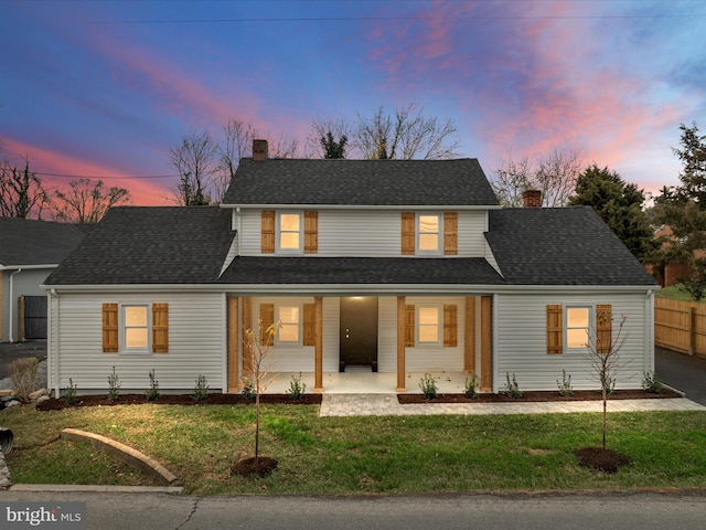 back house at dusk featuring a porch and a yard