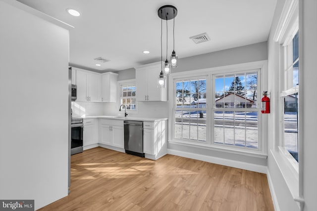 kitchen featuring decorative light fixtures, light hardwood / wood-style floors, white cabinetry, and appliances with stainless steel finishes