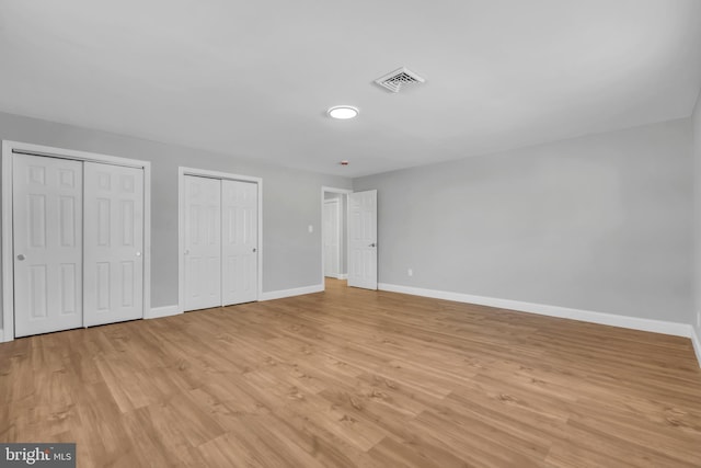 unfurnished bedroom with light wood-type flooring and two closets