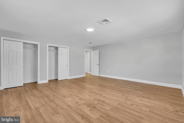 unfurnished bedroom featuring multiple closets and light hardwood / wood-style floors