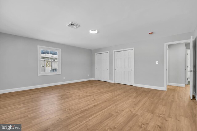 unfurnished bedroom featuring multiple closets and light hardwood / wood-style flooring