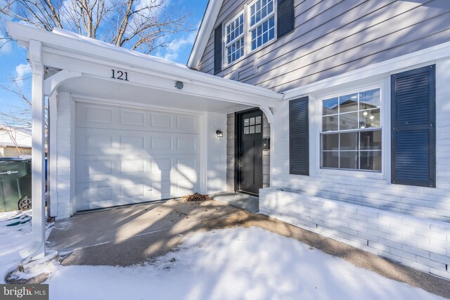 snow covered property entrance with a garage