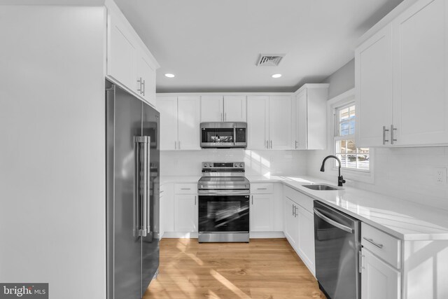 kitchen featuring white cabinets, appliances with stainless steel finishes, light wood-type flooring, and sink