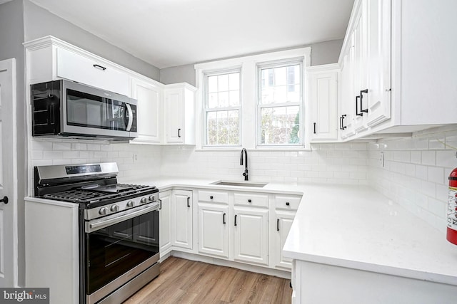 kitchen featuring backsplash, white cabinets, sink, light wood-type flooring, and appliances with stainless steel finishes