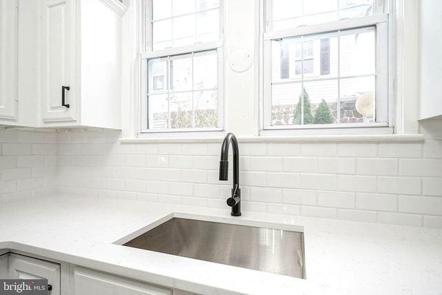 details with sink, light stone countertops, white cabinetry, and backsplash