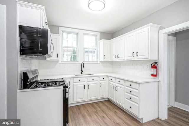 kitchen featuring stove, backsplash, sink, light hardwood / wood-style floors, and white cabinetry