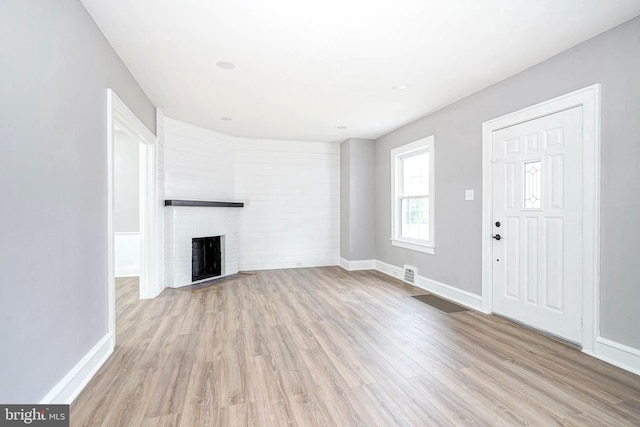 unfurnished living room featuring light hardwood / wood-style floors and a brick fireplace