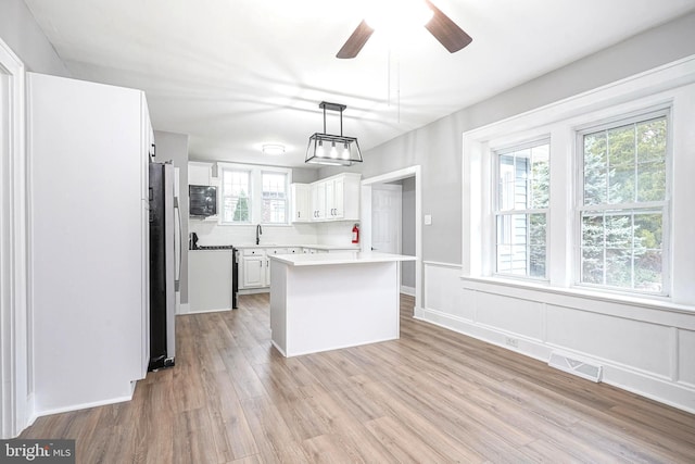 kitchen featuring stainless steel fridge, decorative light fixtures, light hardwood / wood-style flooring, a center island, and white cabinetry