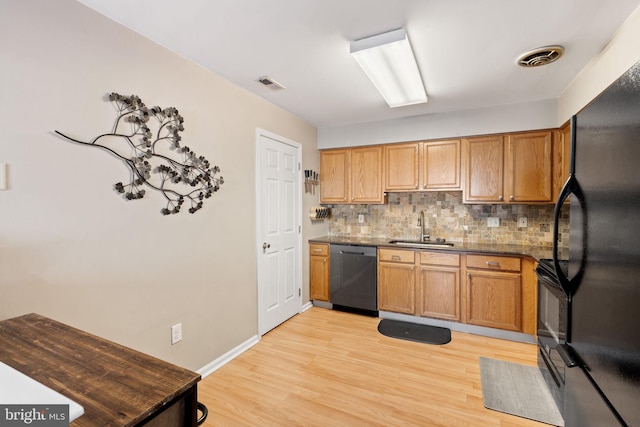 kitchen featuring light wood-type flooring, backsplash, dark stone counters, sink, and black appliances