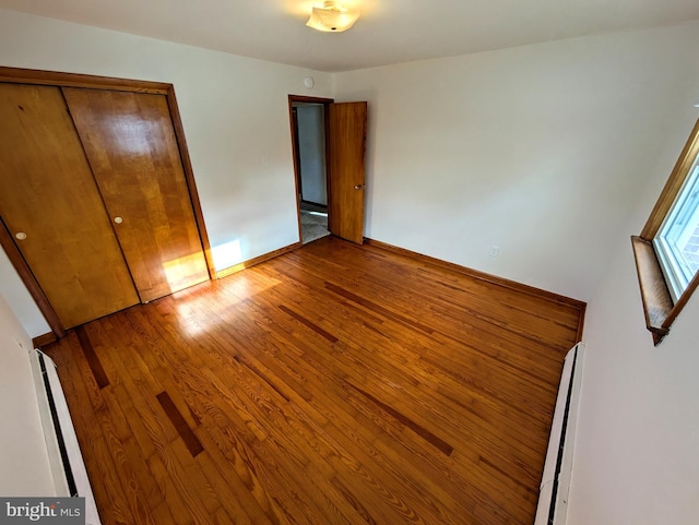 unfurnished bedroom featuring wood-type flooring, a closet, and a baseboard heating unit